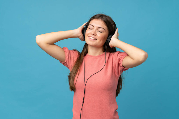 Young woman over isolated blue background using the mobile with headphones - Foto, Imagem