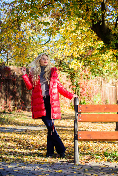 Girl wear red bright warm jacket. Fall fashion concept. Lady attractive fashionista posing in jacket. Woman fashionable blonde with makeup stand in autumnal park. Jacket for fall season concept - Photo, image