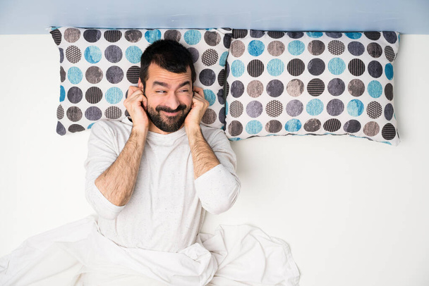 Muž v posteli v top view frustrovaný a zakrývá uši - Fotografie, Obrázek