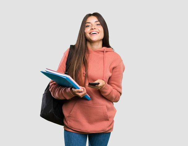 Jonge student vrouw houdt notebooks verzenden van een bericht met de mobiele over geïsoleerde grijze achtergrond - Foto, afbeelding