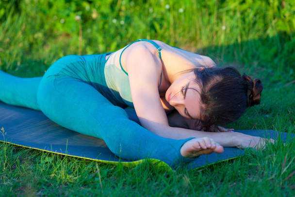 Belle jeune femme faisant de l'exercice d'étirement sur l'herbe verte dans un champ ou un parc
.  - Photo, image