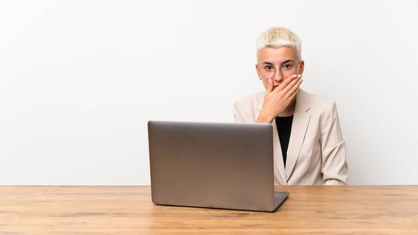Teenager girl with short hair with a laptop covering mouth with hands - Photo, image