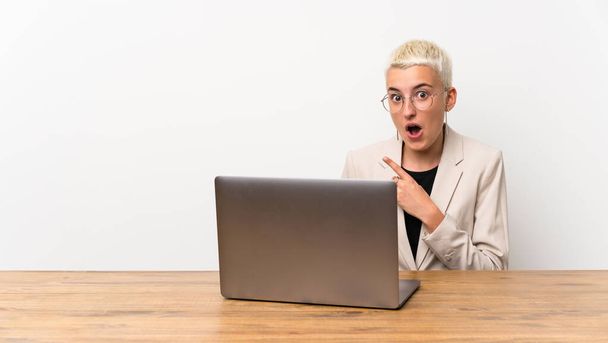 Menina adolescente com cabelo curto com um laptop surpreso e apontando lado
 - Foto, Imagem