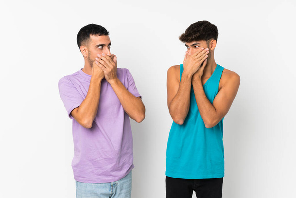 Twee mannen over geïsoleerde achtergrond bedekken mond met handen voor iets ongepasts te zeggen - Foto, afbeelding