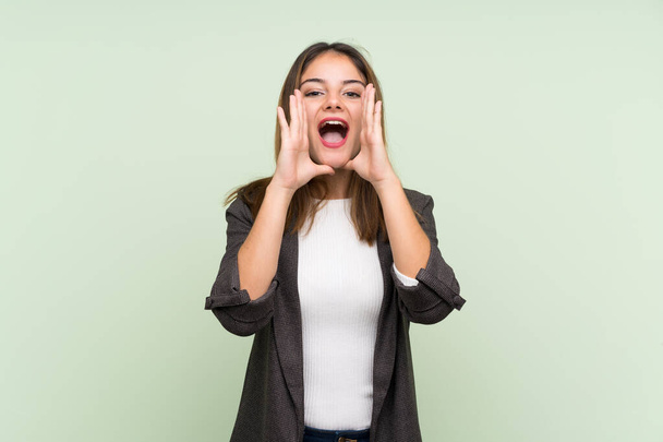 Young brunette girl with blazer over isolated green background shouting and announcing something - Photo, Image