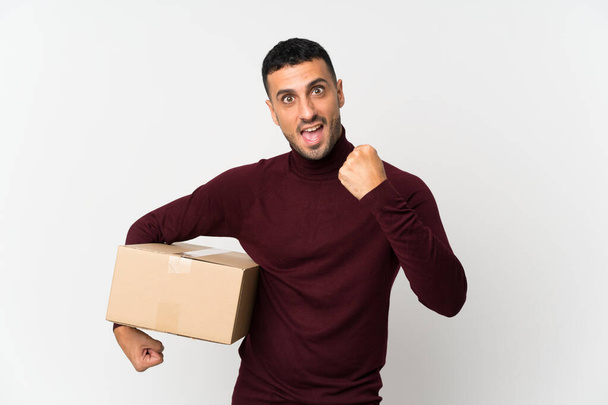 Young man over isolated white background holding a box to move it to another site - Fotoğraf, Görsel
