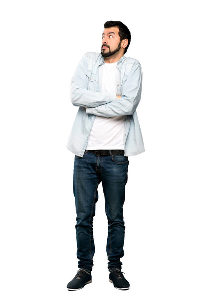 Full-length shot of Handsome man with beard making doubts gesture while lifting the shoulders over isolated white background - Photo, Image