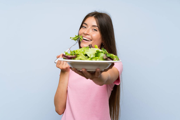 Fiatal nő salátával át elszigetelt kék háttér - Fotó, kép