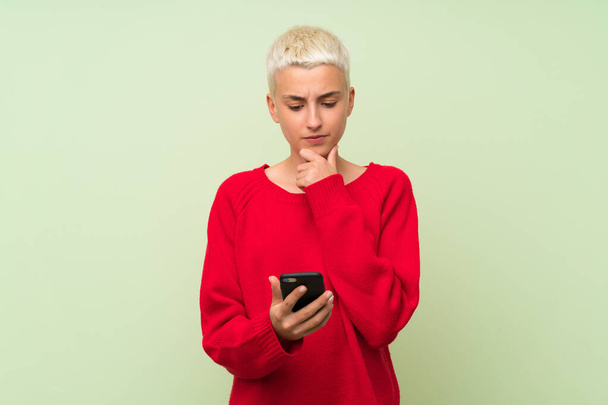 Teenager Mädchen mit weißen kurzen Haaren über grüne Wand denken und eine Nachricht senden - Foto, Bild