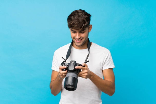 Jeune homme beau sur fond bleu isolé avec une caméra professionnelle
 - Photo, image