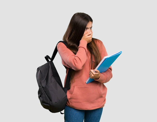 Young student woman holding notebooks covering mouth and looking to the side over isolated grey background - Foto, Bild