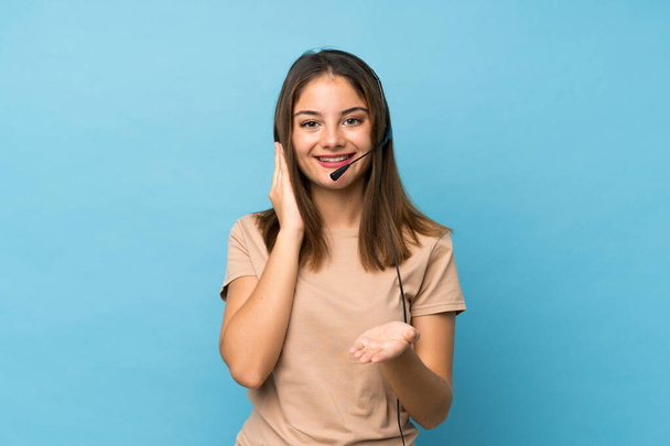 Young brunette girl over isolated blue background working with headset - Φωτογραφία, εικόνα