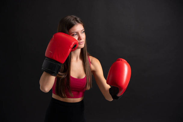 Νεαρή αθλητική γυναίκα με γάντια πυγμαχίας πάνω από απομονωμένο μαύρο φόντο - Φωτογραφία, εικόνα