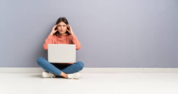 床の上にノートパソコンを持つ若い学生の女の子が不幸で何かに不満。否定的な表情 - 写真・画像