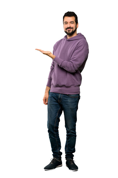 Full-length shot of Handsome man with sweatshirt presenting an idea while looking smiling towards over isolated white background - Photo, image