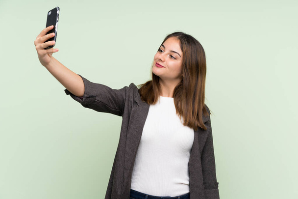 Chica morena joven con chaqueta sobre fondo verde aislado haciendo una selfie
 - Foto, imagen