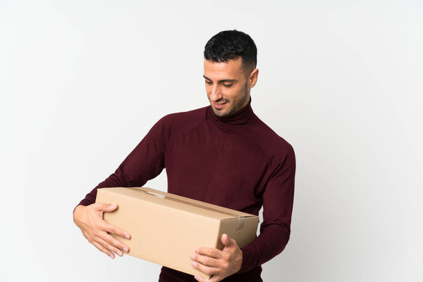 Giovane uomo su sfondo bianco isolato che tiene una scatola per spostarla in un altro sito
 - Foto, immagini