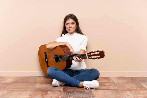 Young woman with guitar sitting on the floor having doubts and with confuse face expression - Foto, Bild