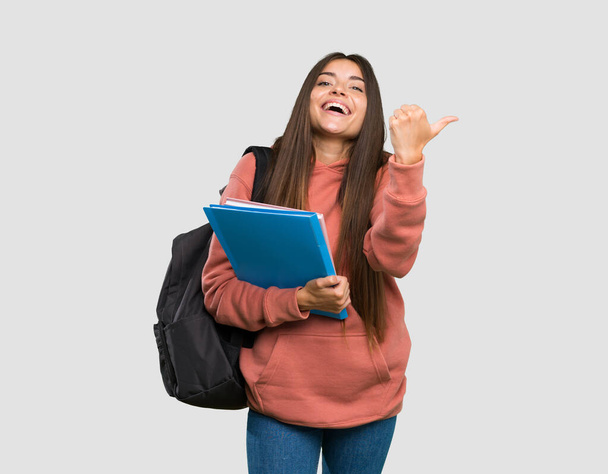 Joven estudiante sosteniendo cuadernos con los pulgares hacia arriba gesto y sonriendo sobre fondo gris aislado
 - Foto, Imagen
