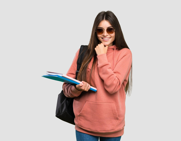 Νεαρή φοιτήτρια που κρατάει σημειωματάρια με γυαλιά και χαμογελά πάνω σε απομονωμένο γκρι φόντο - Φωτογραφία, εικόνα