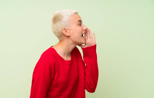 Дівчина-підліток з білим коротким волоссям над зеленою стіною кричить з ротом широко відкритим до бічної
 - Фото, зображення