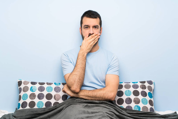 Man in bed bedekken mond met handen - Foto, afbeelding