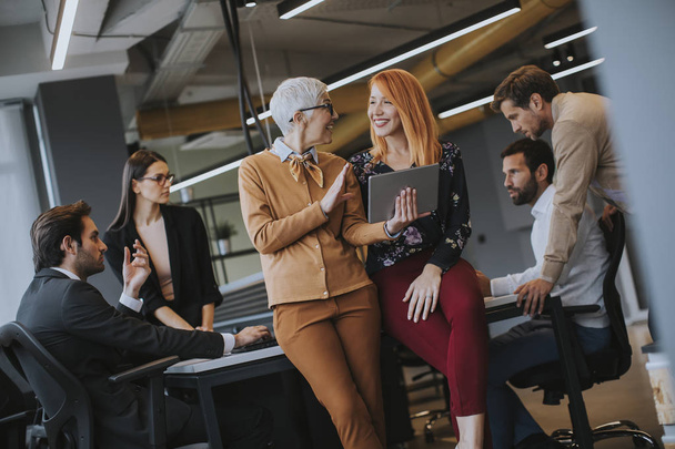 Gelukkige zakenvrouwen werken online samen op een digitale tablet in het bijzijn van een jong team op kantoor - Foto, afbeelding