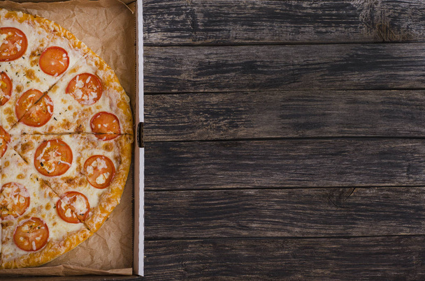 Pizza with cheese and tomatoes in a box with copy space on a dark wooden background. For menus and advertising pizzerias - Photo, image