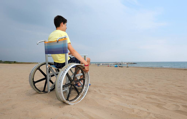 rapaz deficiente em uma cadeira de rodas olha para o mar
 - Foto, Imagem