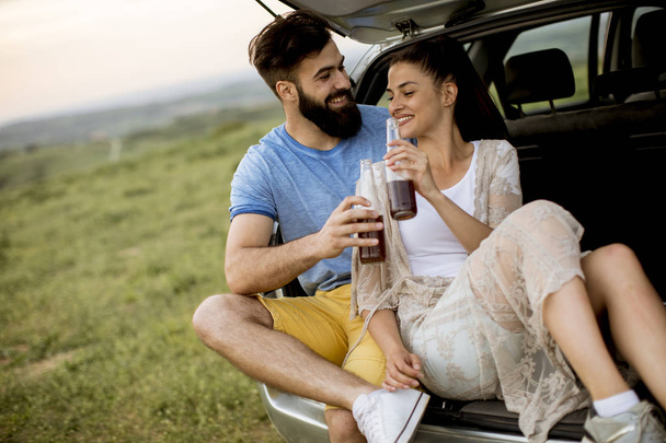Loving young couple sitting in the car trank during trip in the nature - Photo, Image