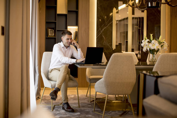 Beau jeune homme d'affaires assis dans une chambre luxueuse devant un ordinateur portable
 - Photo, image