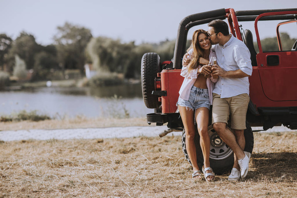 Young woman and man having fun outdoor near red car at hot summer day - Foto, imagen