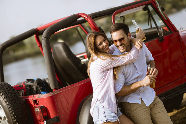 Jonge vrouw en man hebben plezier buiten in de buurt van rode auto op hete zomerdag - Foto, afbeelding