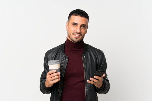 Joven sobre fondo blanco aislado sosteniendo café para llevar y un móvil
 - Foto, Imagen