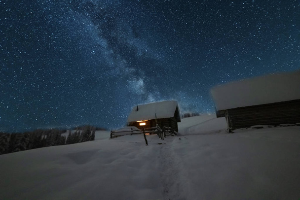 Fairytale landscapes of the winter Carpathian Mountains with a charming milky way in the sky tourist tents and snowy houses in the valleys - Photo, Image