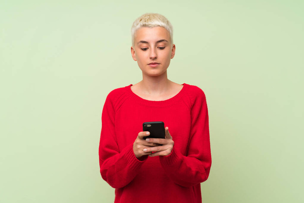 Teini tyttö valkoiset lyhyet hiukset yli vihreä seinä lähettää viestin mobiili
 - Valokuva, kuva