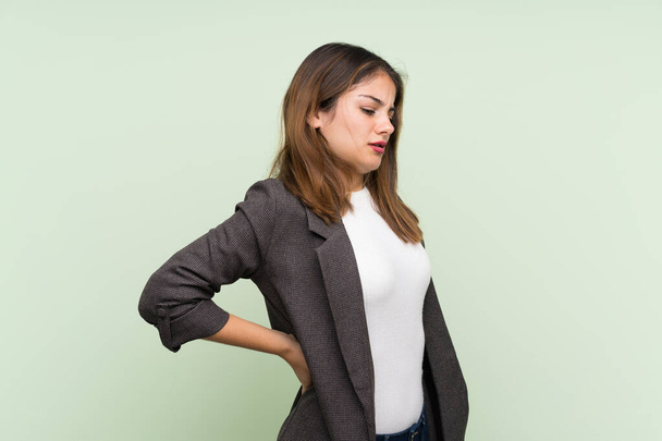 Young brunette girl with blazer over isolated green background suffering from backache for having made an effort - Foto, Imagen