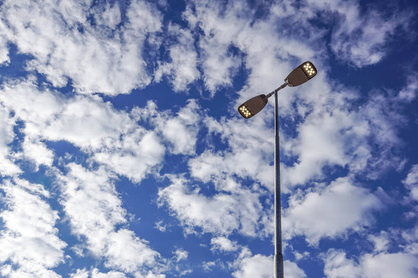 Три светодиодных фонаря, прикрепленных к железному столбу против глубокого голубого неба
 - Фото, изображение