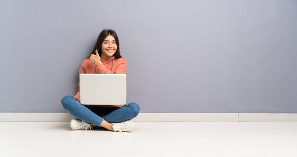 Joven estudiante con un portátil en el suelo dando un gesto de pulgares hacia arriba
 - Foto, Imagen