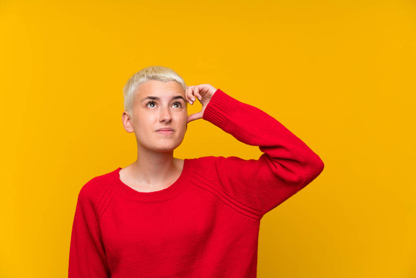 Menina adolescente com cabelos brancos curtos sobre a parede amarela com dúvidas e com expressão facial confusa
 - Foto, Imagem