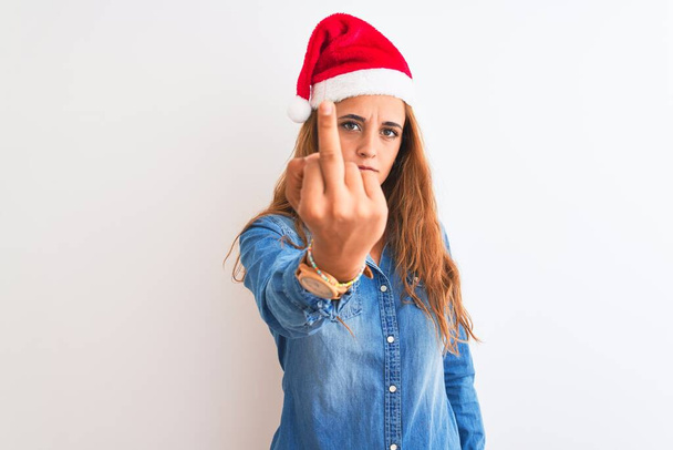 junge schöne rothaarige Frau trägt Weihnachtsmütze über isoliertem Hintergrund zeigt Mittelfinger, unhöflich und unhöflich fuck off Ausdruck - Foto, Bild