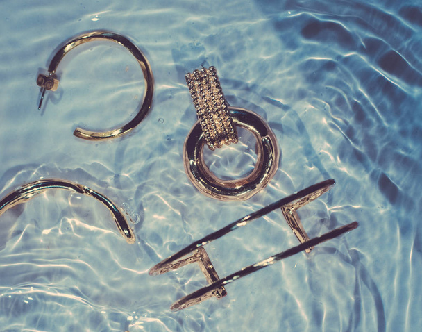Bracciali dorati, orecchini, anelli, gioielli su fondo blu acqua
 - Foto, immagini