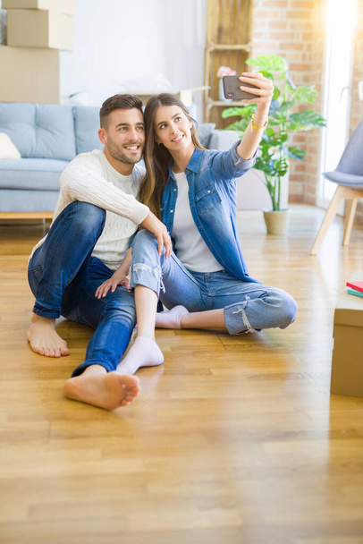 Молодая пара, сидящая на полу нового дома, делает селфи-фото с помощью смартфона, улыбаясь счастливо переезжая в новую квартиру
 - Фото, изображение