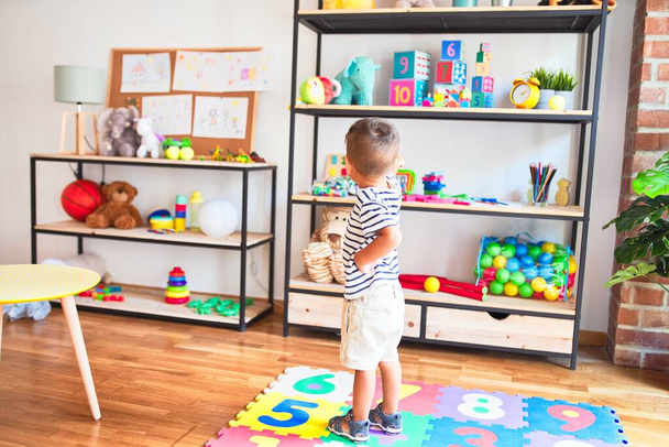Schöner Kleinkind-Junge steht mit vielen Spielsachen im Kindergarten - Foto, Bild