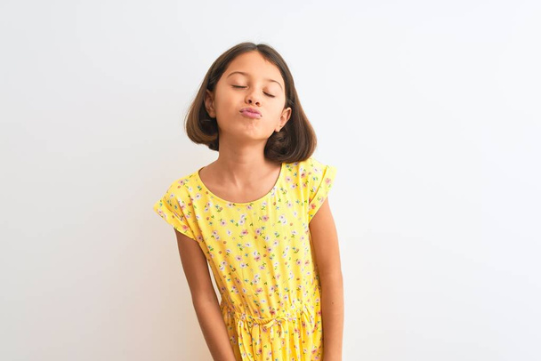 Giovane bella bambina indossa abito floreale giallo in piedi su sfondo bianco isolato guardando la fotocamera soffiando un bacio in aria di essere bella e sexy. Espressione dell'amore
. - Foto, immagini