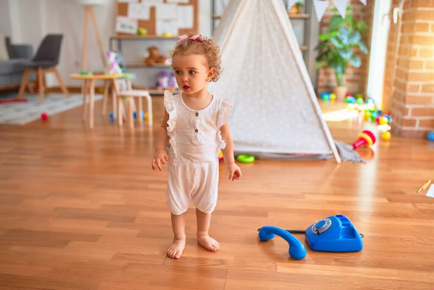 Piękne białe niemowlę bawiące się zabawkami w kolorowym pokoju zabaw. Szczęśliwy i zabawny telefon z vitange w przedszkolu. - Zdjęcie, obraz