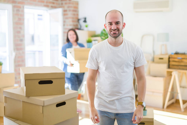 Молодая пара вокруг картонных коробок переезжает в новый дом, лысый мужчина стоит дома с счастливой и прохладной улыбкой на лице. Счастливчик
. - Фото, изображение