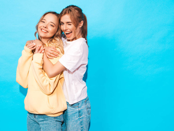 Deux jeunes belles filles blondes hipster souriantes en t-shirt coloré d'été à la mode. Sexy femmes insouciantes posant près du mur bleu. Modèles positifs s'amuser
  - Photo, image