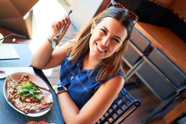junge schöne Frau sitzt im Restaurant und genießt den Sommerurlaub und isst leckeres Essen - Foto, Bild