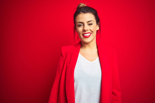 Young beautiful business woman standing over red isolated background winking looking at the camera with sexy expression, cheerful and happy face. - Fotografie, Obrázek